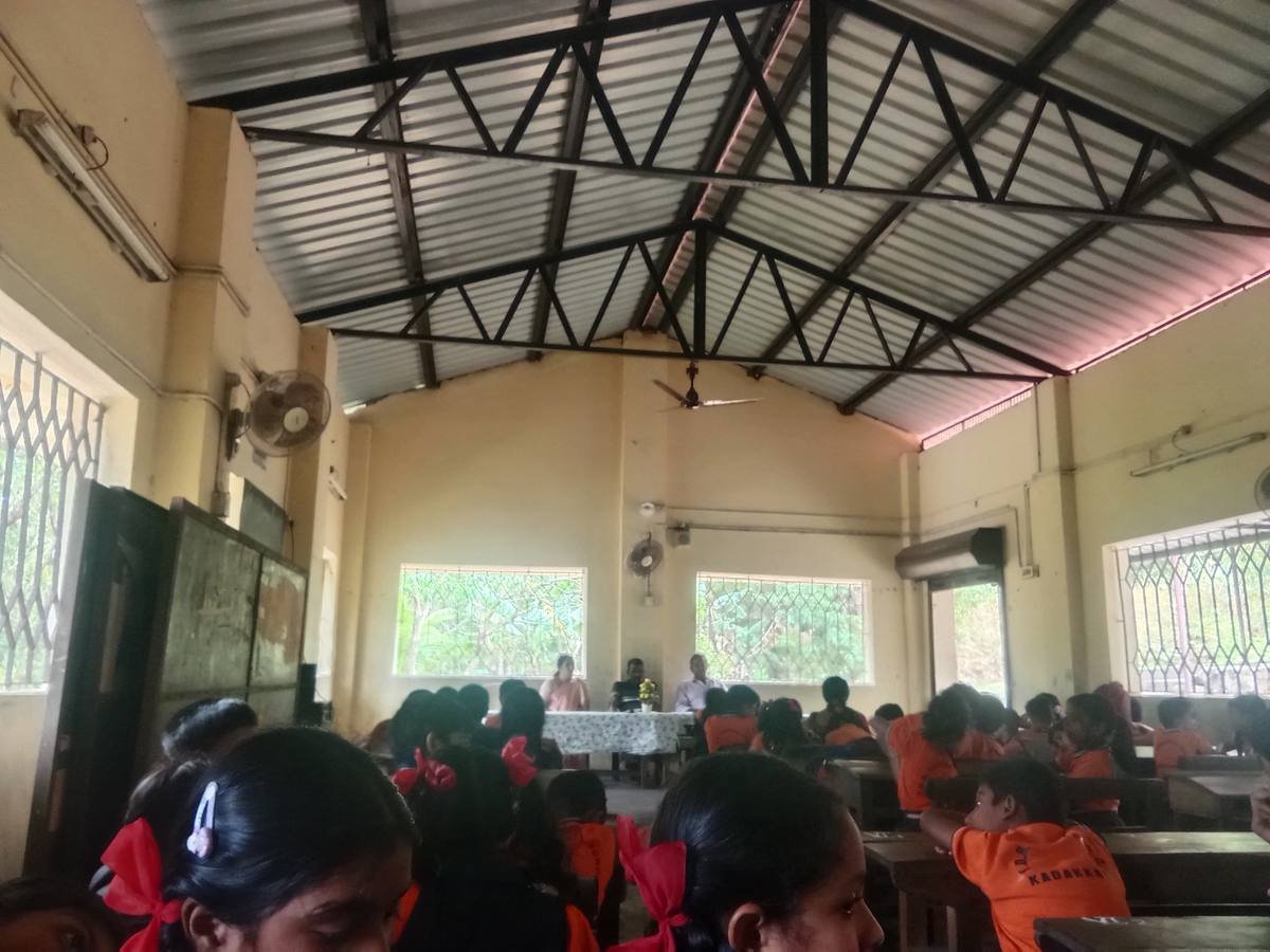 The school hall during the session, pupils at their benches facing the table under the steel roof trusses.