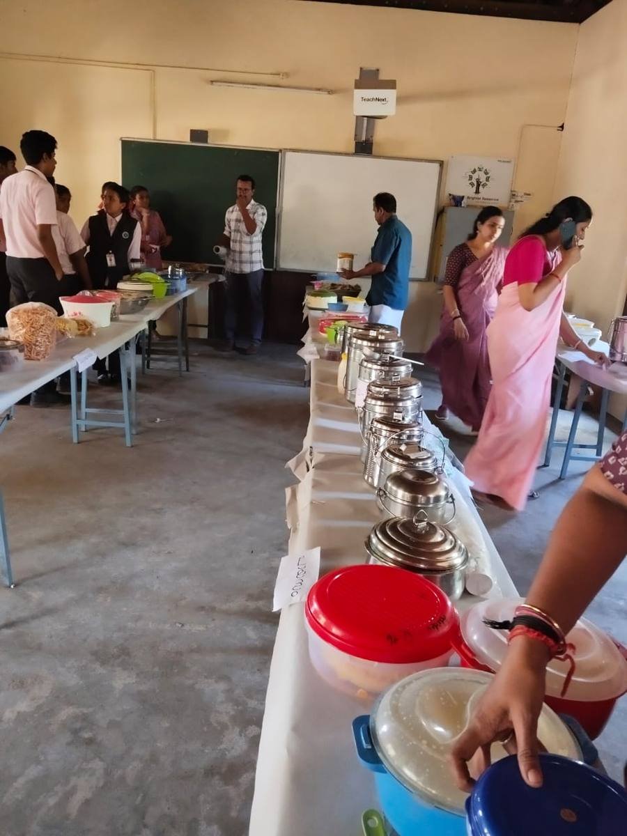 A long line of tiffin carriers and covered dishes down the table, each with a paper label.