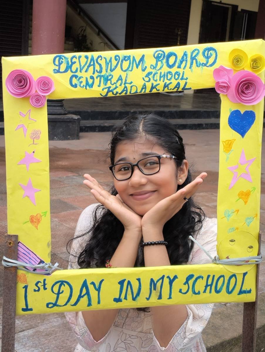 A pupil in glasses resting her chin on her hands inside the hand-made "1st day in my school" frame.