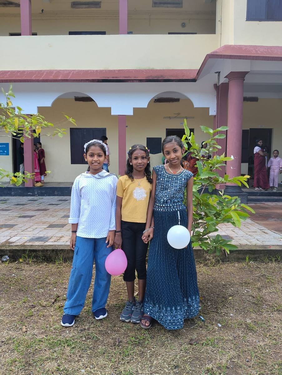 Three pupils holding balloons on the grass in front of the school block.