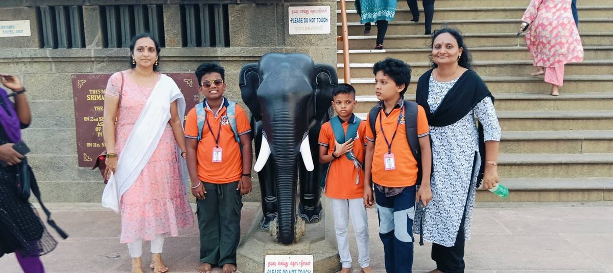 Pupils and two teachers beside a carved stone elephant at the foot of a flight of steps.