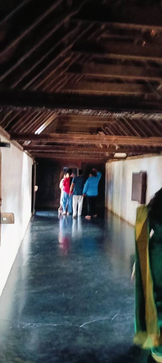 Visitors at the far end of a palace corridor under its carved wooden ceiling.