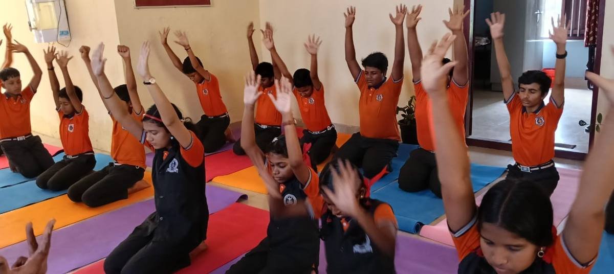 Senior pupils in orange PT uniform kneeling with both arms raised.