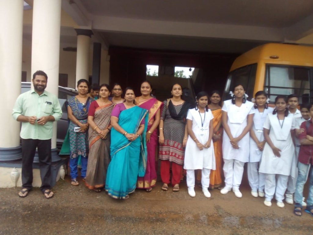 Staff and students standing beside the school bus under the portico.